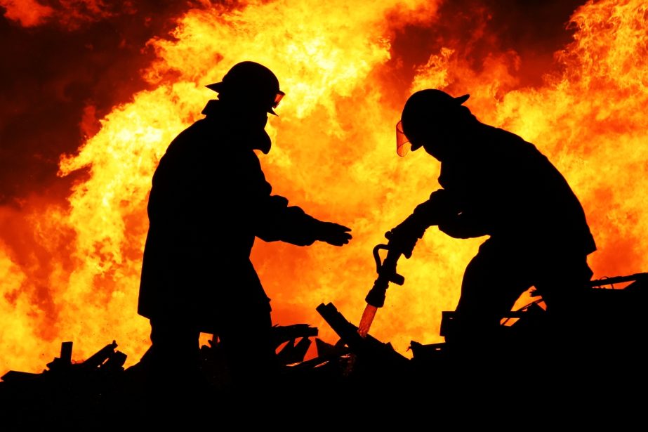 Silhouette of Firemen fighting a raging fire with huge flames of burning timber